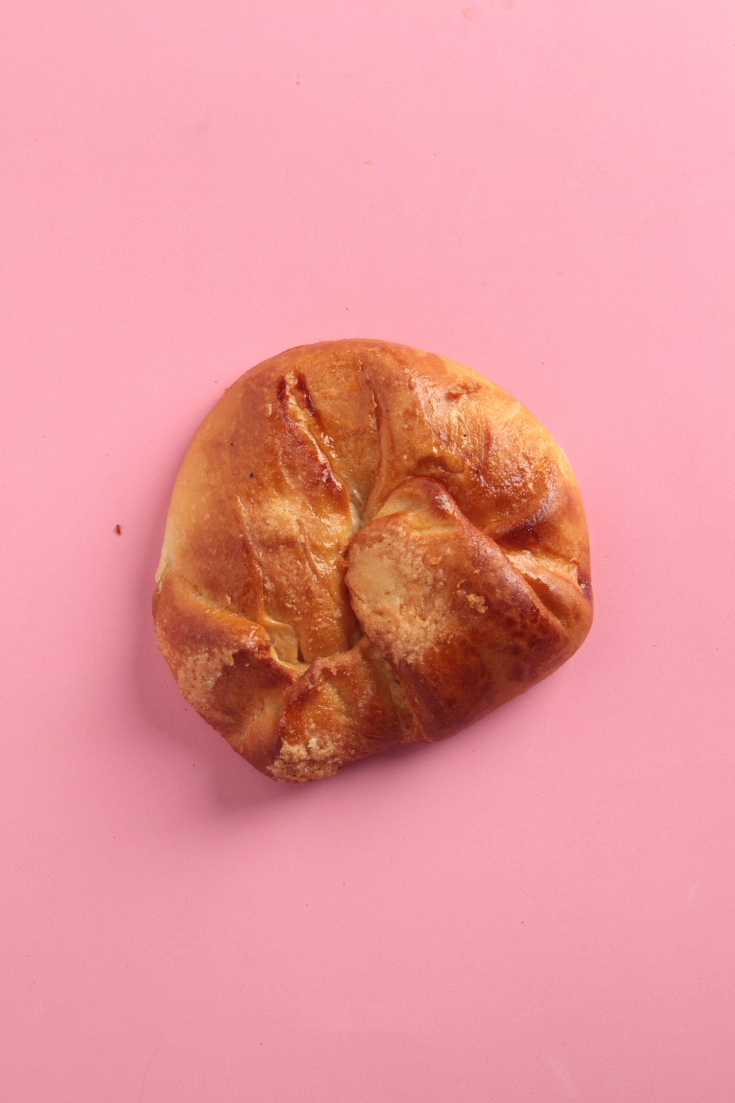 A freshly baked honey bun with a glossy, golden-brown crust photographed against a pastel pink background. Photo by Robcarbo, licensed via Depositphotos.