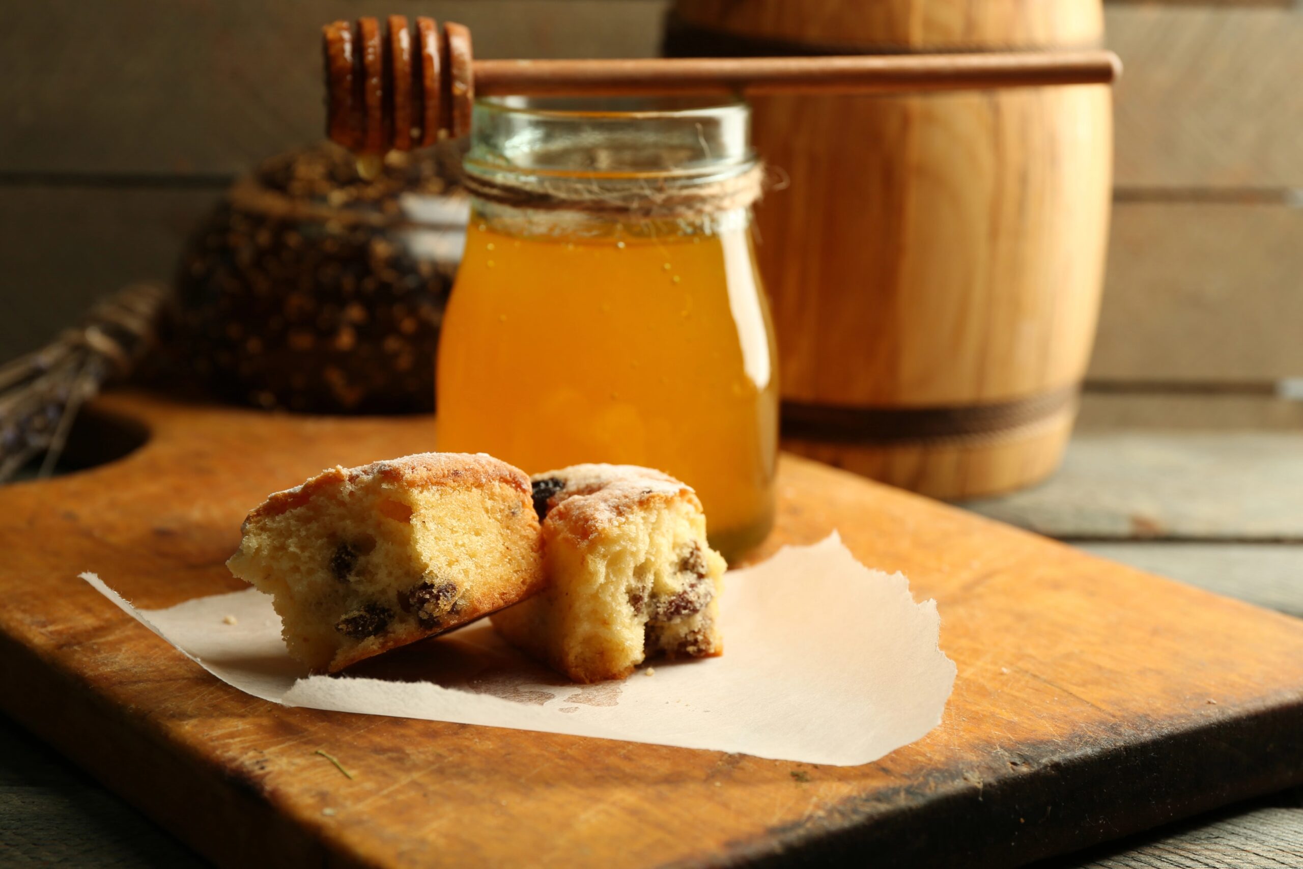 Slices of fresh sweet bread displayed on parchment paper alongside a jar of golden honey on a wooden cutting board, creating a warm, rustic dessert scene. Photo by belchonock, licensed via Depositphotos.
