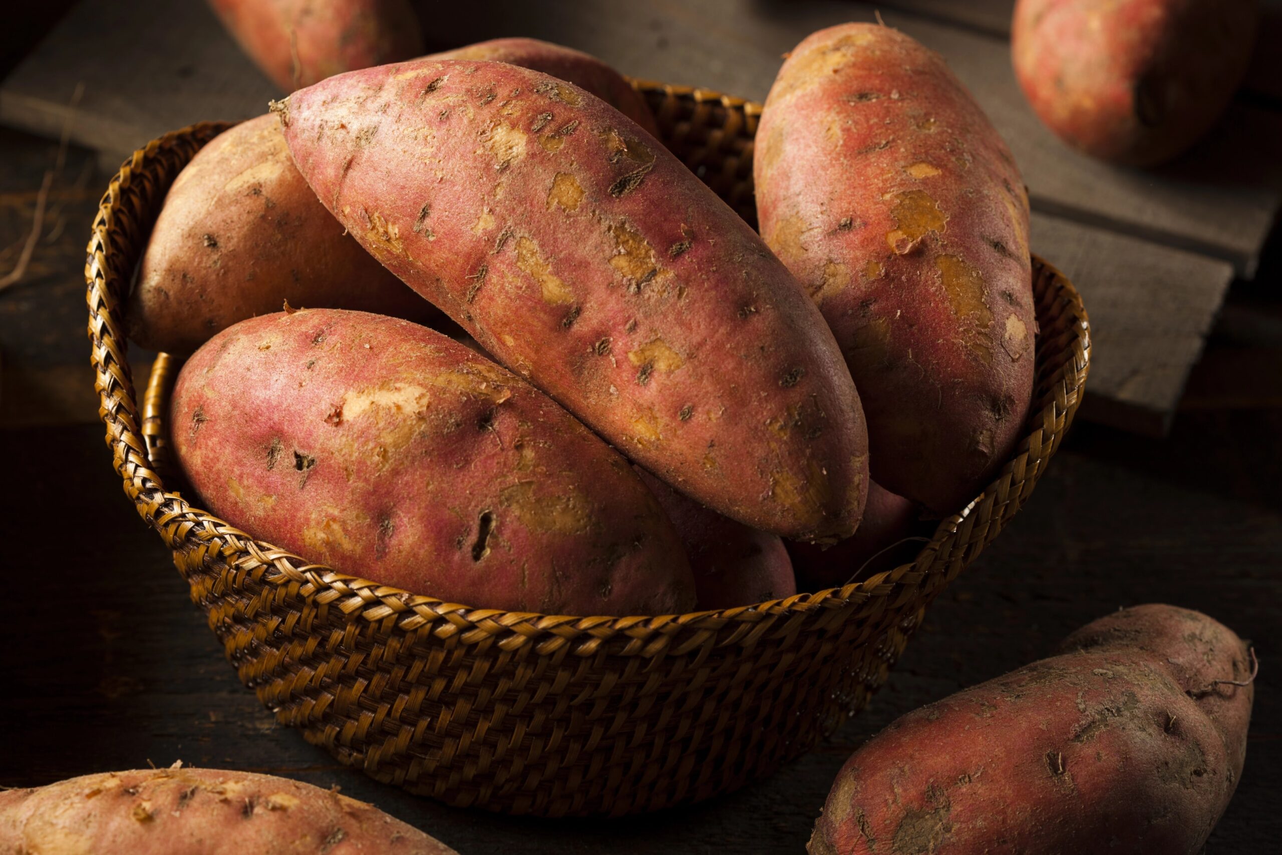 A basket filled with organic raw sweet potatoes resting on a rustic wooden surface, highlighting their natural texture and earthy color. Photo by bhofack2, licensed via Depositphotos.