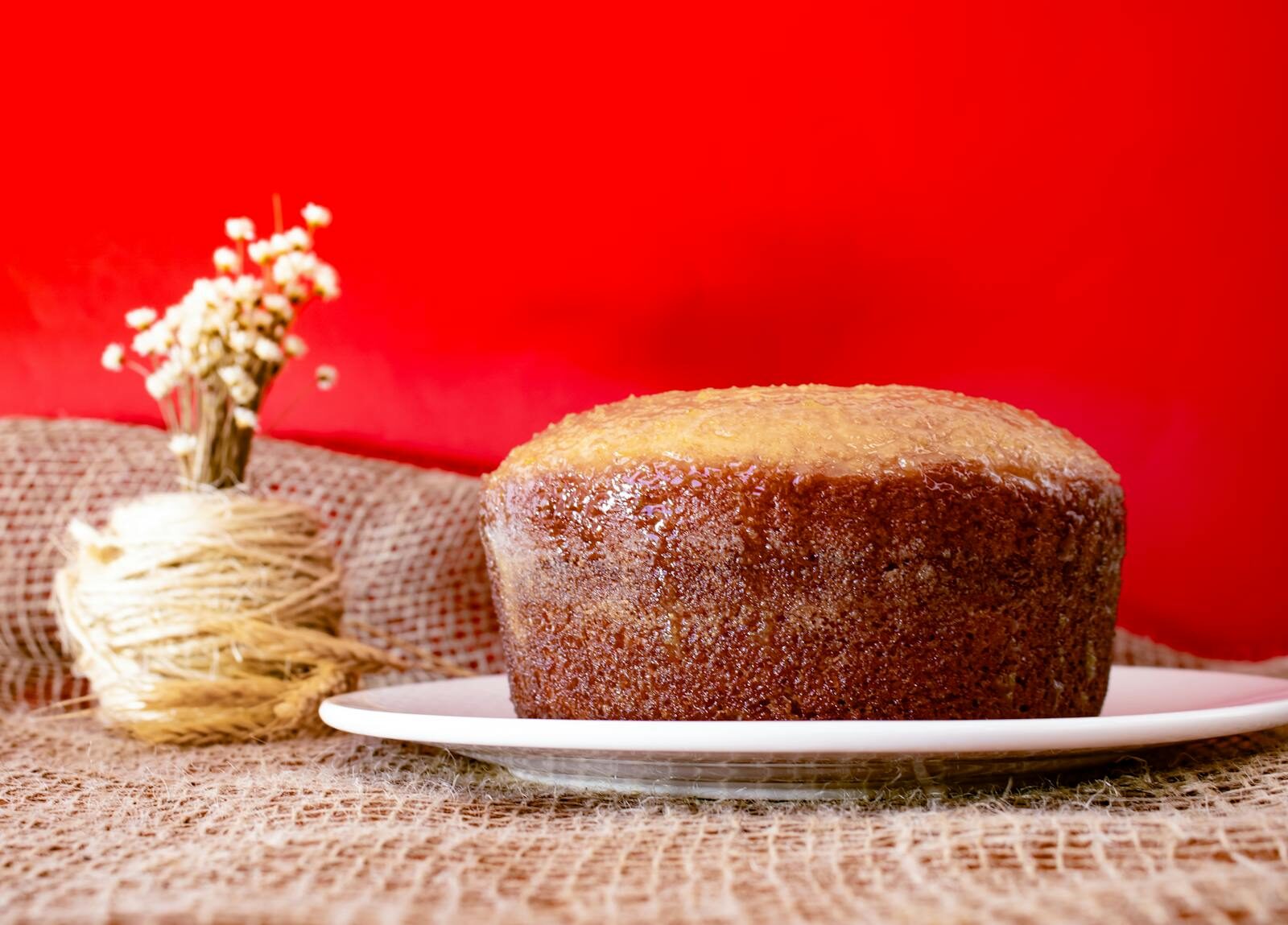 Moist homemade cake on a white plate with rustic burlap and red backdrop, perfect for food photography.