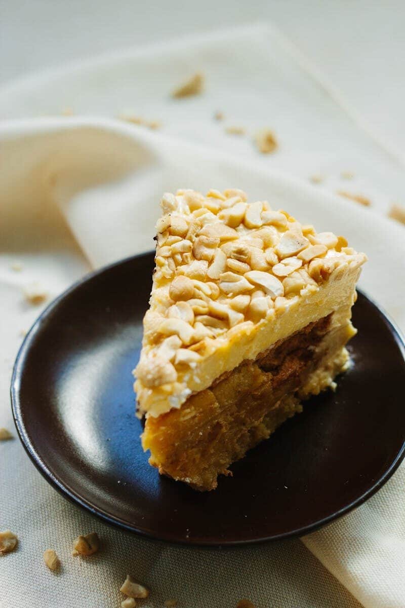 A delicious slice of nut-covered cake served on a dark plate.