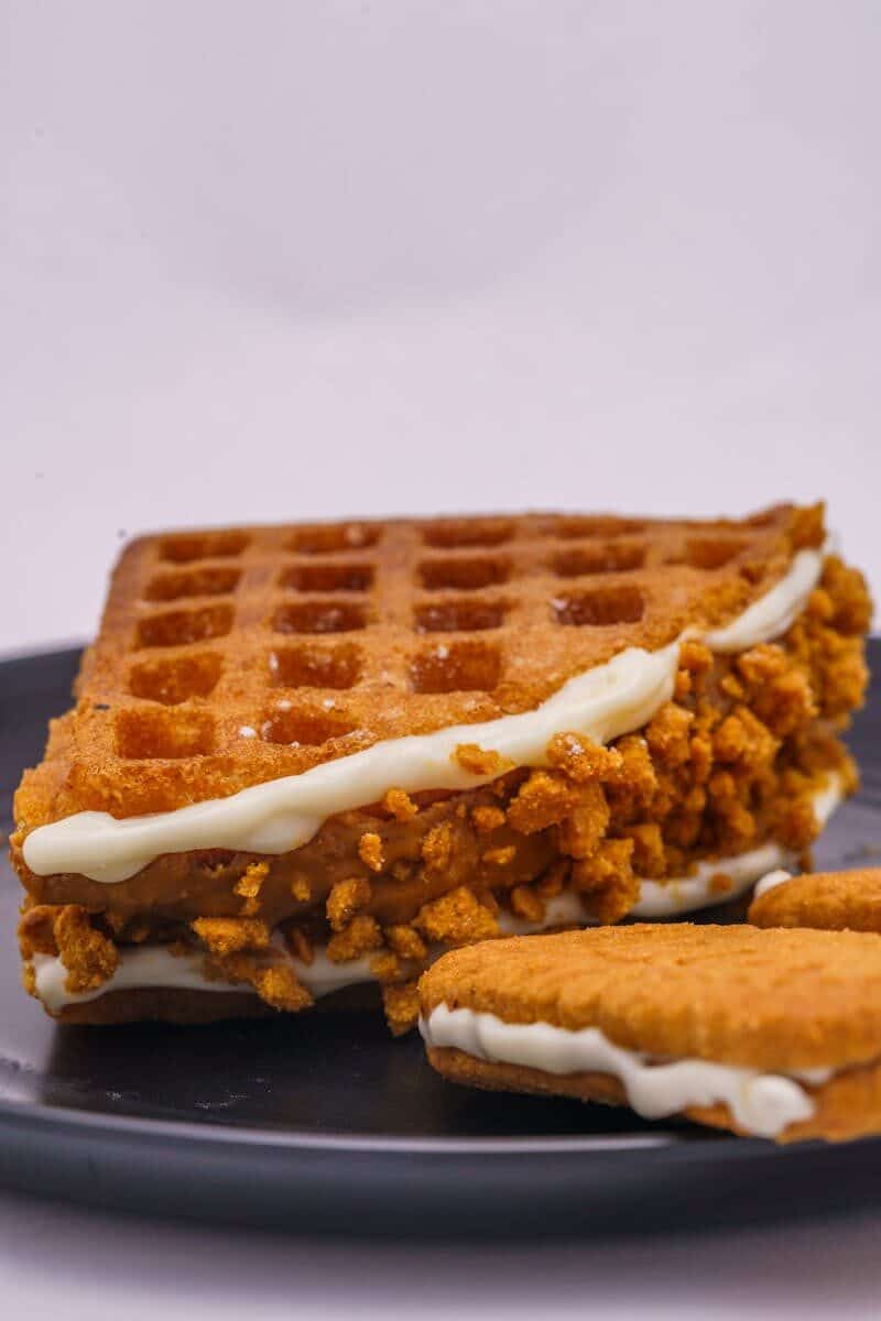Close-up of a waffle ice cream sandwich with crumbs and cream on a black plate.