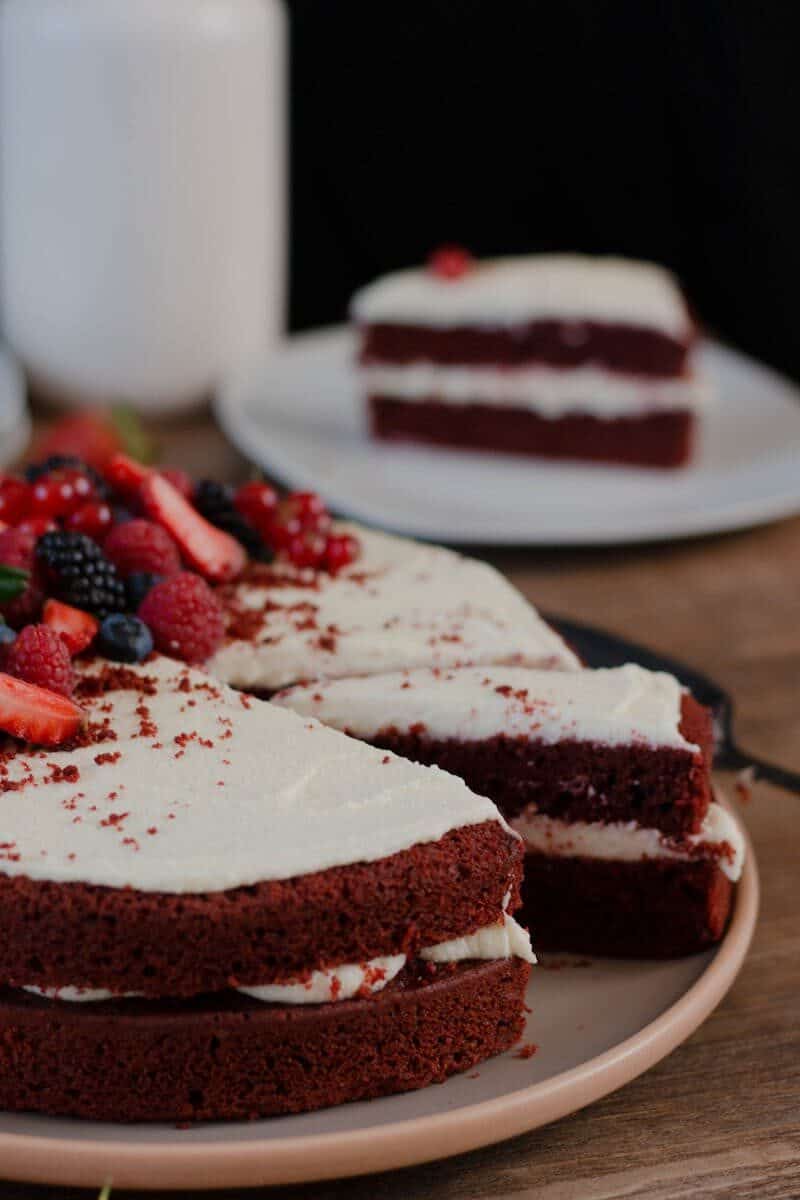 Delicious red velvet cake slice with creamy frosting and mixed berries on top.