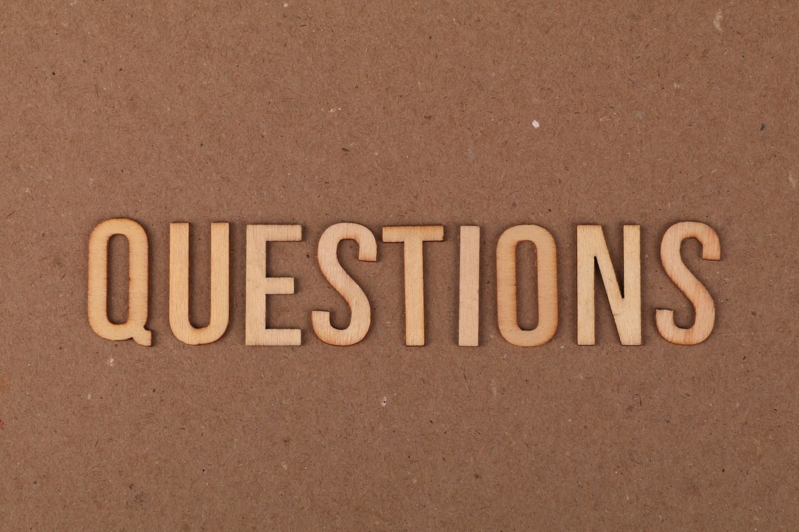 Wooden letters spelling the word "QUESTIONS" on a cardboard background, providing a neutral copyspace.
