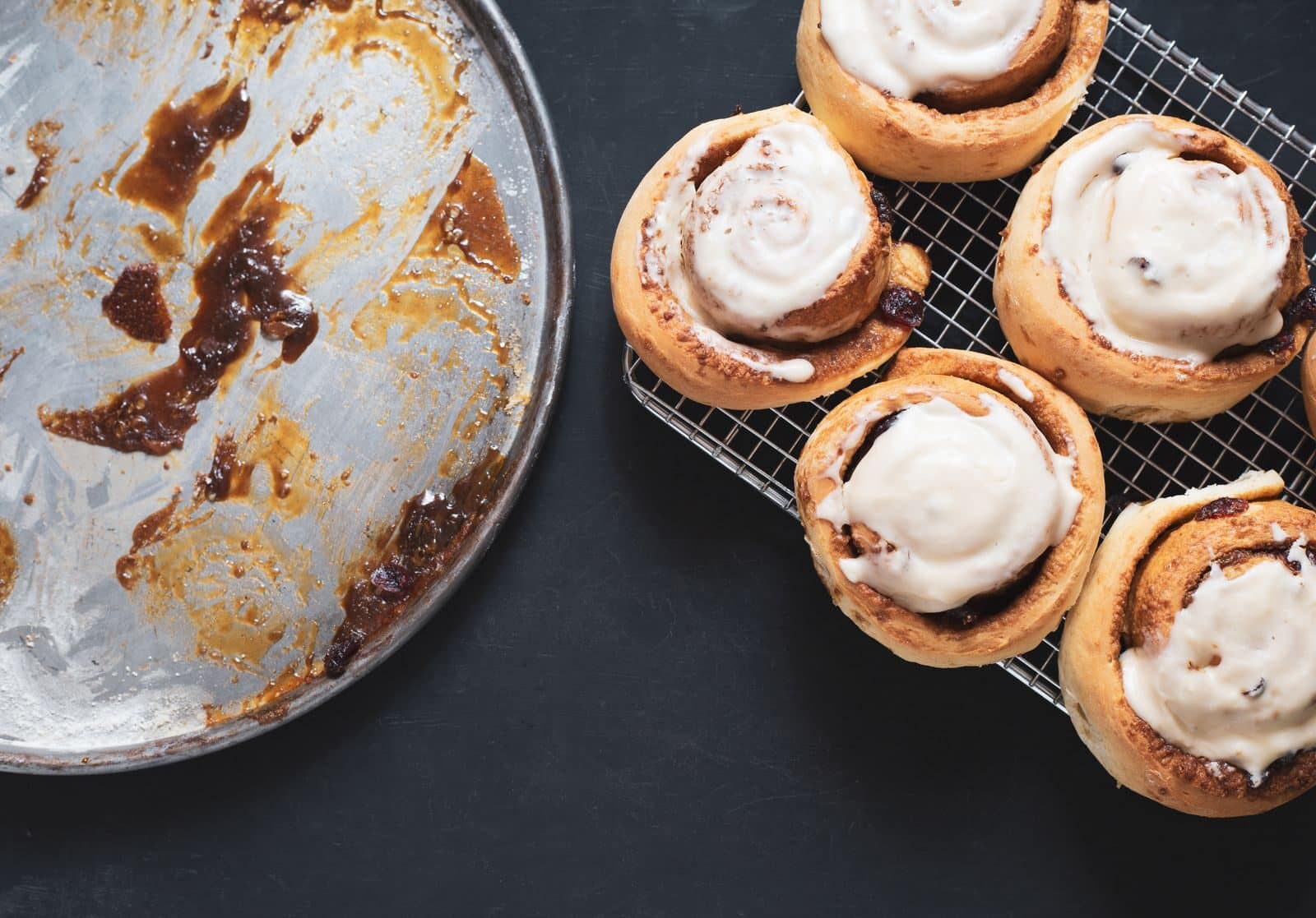 Delicious homemade cinnamon rolls with icing on cooling rack next to an empty baking tray.